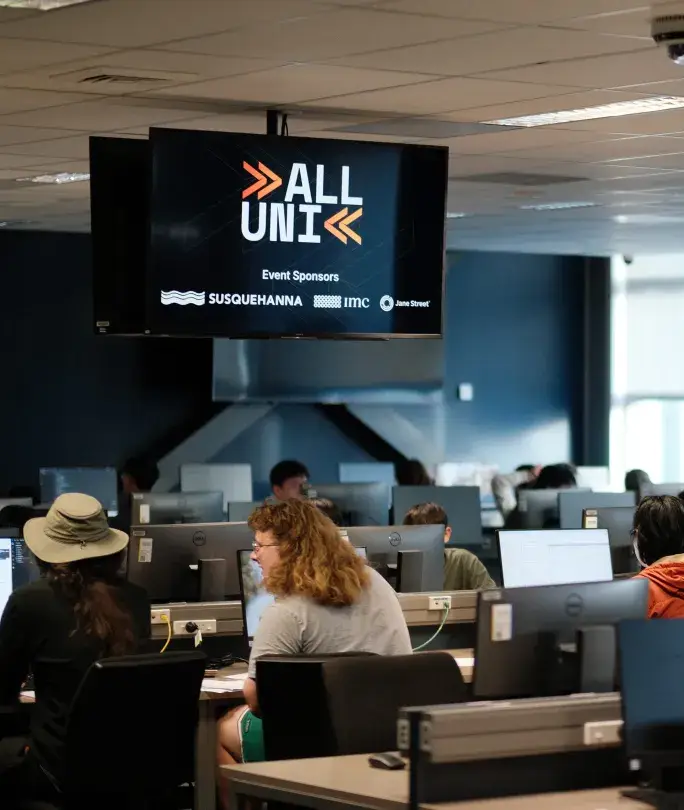 Students in a computer lab competing in a contest, with AllUni branding on an overhead TV